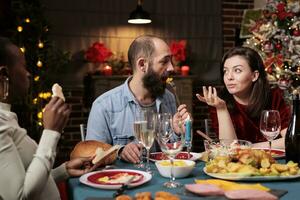 coppia festeggiare Natale vigilia con famiglia, recitazione romantico a cena tavolo con le persone. diverso persone godendo raccolta con fatti in casa cibo e alcool per celebrare natale vacanza evento. foto