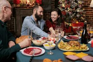 carino persone incontro famiglia a casa su Natale vigilia vacanza, raccolta in giro tavolo con persone per mangiare pasto e bevanda alcol. giovane persone parlando per parenti durante dicembre festa. foto