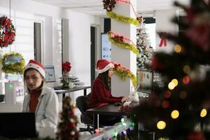 diverso attività commerciale squadra Lavorando su Natale stagione nel decorato ufficio. focalizzata dipendenti indossare natale cappelli, guardare al di sopra di statistica grafici, ricercando dati nel festivo posto di lavoro foto