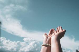 le mani della donna si mettono insieme come pregare davanti allo sfondo del cielo blu. foto