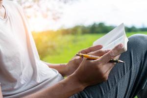 in un parco pubblico, un uomo sta scrivendo a mano in un piccolo taccuino bianco per prendere nota di qualcosa che non vuole dimenticare o per fare una lista di cose da fare per il futuro.