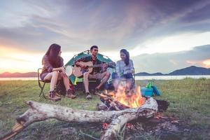 gruppo di viaggiatori che si accampano e fanno picnic e suonano musica insieme. sfondo di montagna e lago. persone e stile di vita. attività all'aperto e tema del tempo libero. zaino in spalla ed escursionista. alba e crepuscolo foto