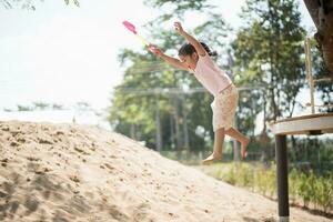 asiatico ragazza bambini salto e giocando sabbia su il terreno di gioco nel il bar per bambini. poco ragazza giocando nel il sabbia su il terreno di gioco. salutare attivo bambino all'aperto giochi Giochi concetto. foto