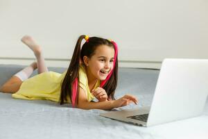 carino poco ragazza utilizzando il computer portatile a casa. formazione scolastica, in linea studia, casa studiando, distanza apprendimento, scolara bambini stile di vita concetto foto