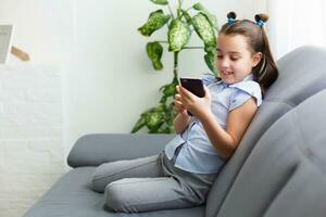 distanza apprendimento, in linea formazione scolastica per bambini. poco ragazza studiando a casa nel davanti di il smartphone. bambino Guardando in linea cartoni animati, bambini computer dipendenza, genitoriale controllo. quarantena a casa foto