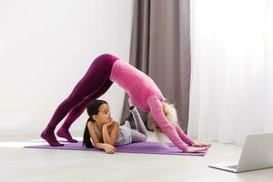 madre e figlia praticante in linea yoga lezione a casa a quarantena solitudine periodo durante coronavirus pandemia. famiglia fare sport insieme in linea a partire dal casa. salutare stile di vita foto