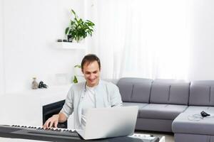 un' uomo apprendimento per giocare pianoforte in linea con un' computer soggiorno a casa. concetti di se stesso insegnato, soggiorno a casa e Lavorando in linea foto