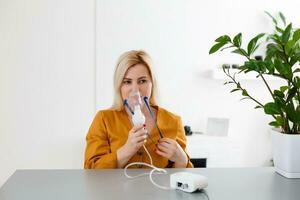 donna fa inalazione nebulizzatore a casa. Tenere un' maschera nebulizzatore inalando vapore spray il medicazione in il tuo polmoni malato paziente. autotrattamento di il respiratorio tratto utilizzando inalazione nebulizzatore foto