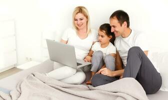 contento famiglia bugie su letto e Guardando qualcosa su il computer portatile. foto