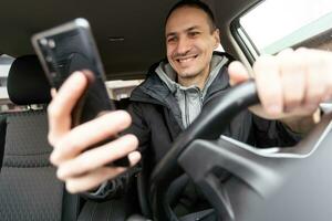 bello giovane uomo nel denim camicia urgente touch screen su auto multimedia pannello, commutazione mutevole Radio stazione. foto