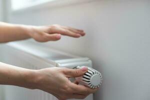 un' donna di mano detiene il riscaldamento termostato maneggiare. riscaldamento servizio costo concetto, utilità prezzo aumentare foto