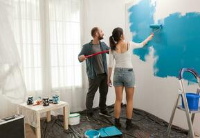 Gli amanti pittura parete utilizzando rullo dipingere spazzola e blu colore. casa durante ristrutturazione, decorazione e la pittura. interno appartamento miglioramento Manutenzione. rullo, scala per Casa riparazione foto