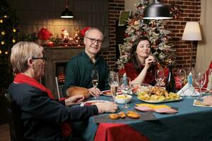 vecchio persona a tavolo su natale con famiglia mangiare tradizionale pasto e festeggiare Natale vacanza a casa. anziano persone ospitando festivo natale cena evento durante inverno stagione. foto