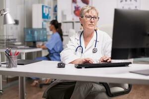 esperto medico utilizzando computer nel clinica Consiglio dei ministri e infermiera digitando su pc nel il sfondo. foto