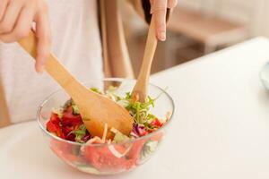 vicino su di casalinga mani miscelazione insalata ingredienti nel cucina. foto
