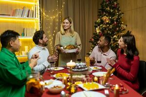 multietnico gruppo di contento amici avendo Natale cena ,insieme a casa insieme. vacanze e celebrazione, concetto. ringraziamento giorno il hostess volontà servire il tacchino. riunione festa foto