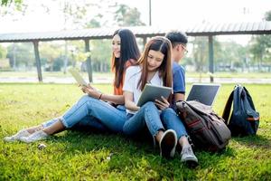 gruppo di studenti universitari asiatici che utilizzano tablet e laptop sul campo in erba all'aperto. tecnologia e concetto di apprendimento dell'istruzione. tecnologia del futuro e moderno concetto di intrattenimento. tema edutainment foto