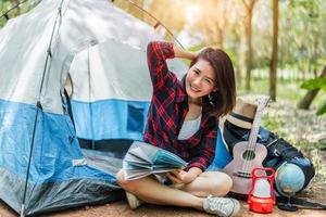 bella donna asiatica che gioca ukulele davanti alla tenda da campeggio nei boschi di pini. concetto di persone e stili di vita. tema avventura e viaggio foto