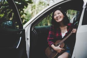 bellezza asiatica donna sorridente e divertirsi all'aperto estate con ukulele in macchina bianca. viaggio del concetto di fotografo. stile hipster e tema donna solista. stile di vita e felicità tema della vita foto