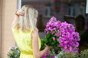 un' bellissimo bionda donna con un' enorme mazzo di fiori ammira sua riflessione nel un' negozio finestra. foto