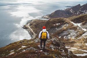 uomo viaggiatore con uno zaino giallo in piedi sulle rocce sullo sfondo del mare e delle montagne foto