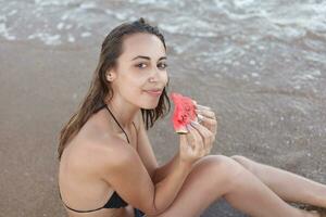 estate vacanza - giovane ragazza mangiare fresco anguria su sabbioso spiaggia foto