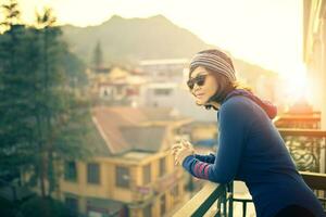 minore in viaggio donna in piedi al di fuori edificio terrazza e guardare per destinazione scena contro bellissimo sole salire foto