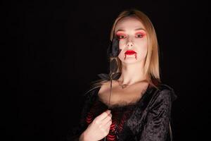 bellissimo biondo vampiro donna con un' rosa al di sopra di nero sfondo per Halloween. foto