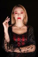 biondo donna vestito su piace un' vampiro con sangue su il suo labbra al di sopra di nero sfondo. Halloween costume. foto