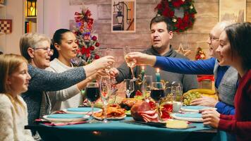 famiglia con diverso età tintinnante bicchieri con Champagne festeggiare Natale. tradizionale festivo Natale cena nel multigenerazionale famiglia. godendo natale pasto festa nel decorato camera. grande famiglia riunione foto