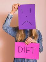 donna copertura sua viso con triste viso su carta mentre Tenere carta con parola dieta. foto