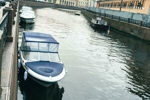 Barche e motoscafi ormeggiato nel un' fiume città canale con urbano paesaggio nel il sfondo foto