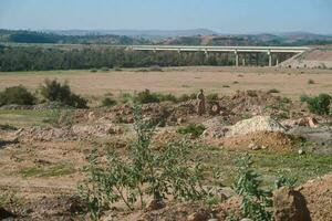 un' Visualizza di un' sporco campo con un' ponte nel il sfondo foto