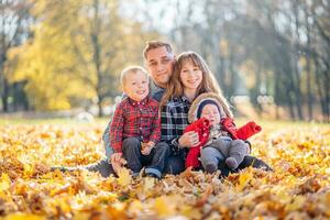 un' giovane famiglia si siede nel il parco su un' frondoso, soleggiato autunno giorno. foto