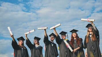 allegro laureati posa con sollevato diplomi su un' soleggiato giorno. foto