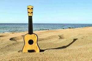 un' di legno ukulele si siede su il sabbia vicino il oceano foto