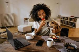 giovane donna nera che gioca con il suo cane mentre fa colazione foto
