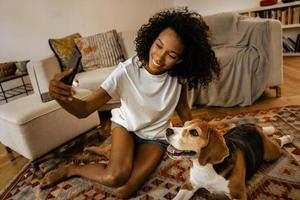 donna nera che si fa un selfie con il suo cane mentre è seduta sul pavimento foto