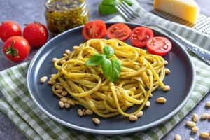 tradizionale italiano spaghetti pasta con pesto salsa e fresco basilico le foglie nel nero ciotola foto