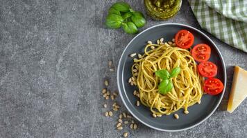 tradizionale italiano spaghetti pasta con pesto salsa e fresco basilico le foglie nel nero ciotola foto