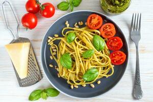 tradizionale italiano spaghetti pasta con pesto salsa e fresco basilico le foglie nel nero ciotola foto