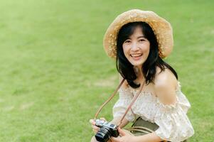 ritratto di asiatico giovane donna viaggiatore con tessitura cappello e cestino e un' telecamera su verde pubblico parco natura sfondo. viaggio viaggio stile di vita, mondo viaggio esploratore o Asia estate turismo concetto. foto