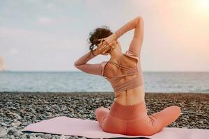 donna mare pilates. sportivo contento mezzo anziano donna praticante fitness su spiaggia vicino mare, sorridente attivo femmina formazione con squillare su yoga stuoia fuori, godendo salutare stile di vita, armonia e meditazione foto