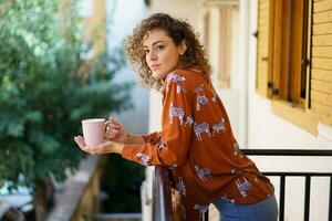 giovane donna con caffè tazza pendente su balcone di Casa foto
