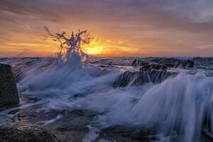 sorprendente spruzzo di acqua di mare a Alba su il riva di il nero mare. bellissimo movimento sfocatura mare onde al di sopra di il rocce. Basso angolo Visualizza foto