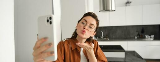 ritratto di elegante bellissimo donna a casa, video chat su smartphone, si connette per in linea incontro a partire dal sua vivente camera, stile di vita sociale media blogger record un' video su mobile Telefono foto