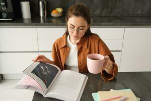 distanza apprendimento. giovane donna a casa, alunno studiando a casa e potabile Tè, lettura sua opera prenotare, revisione per esame foto