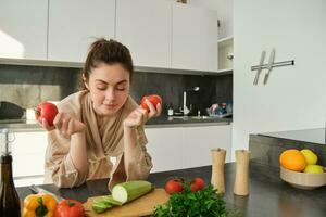 ritratto di donna cucinando a casa nel il cucina, Tenere pomodori, preparazione delizioso fresco pasto con la verdura, in piedi vicino chopping tavola foto
