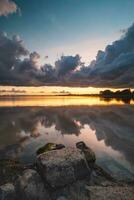 Perfetto tramonto su il sponde di lago gooimer vicino almere. il viola-arancione inferno si illumina il passaggio nuvole e riflette su il calma superficie. bellezza di Olanda foto