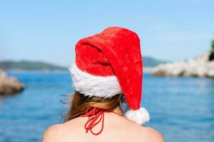 giovane ragazza nel Santa cappello e nel un' costume da bagno a il mare. indietro Visualizza. vacanza concetto per nuovo anno e Natale vacanze. avvicinamento. foto